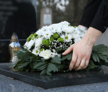 Kobieta kładzie białe kwiaty na grobie na cmentarzu, spokojna chwila pożegnania.